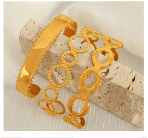 Detail view of gold Cuban chain bracelets and C-shaped cuffs on textured stone and silk