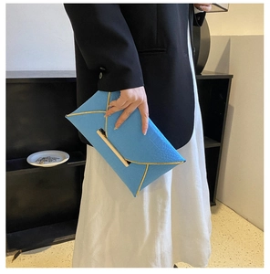 Détail d'une pochette enveloppe bleue avec bordure dorée et cuir texturé sur un mannequin
