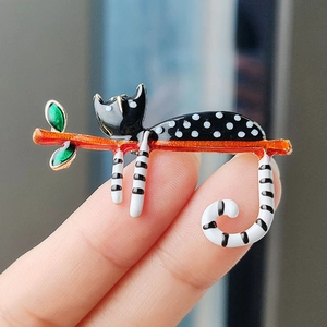 Cute spotted black cat enamel brooch perched on orange branch with green leaves