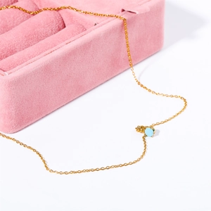 Detail shot of a golden titanium steel necklace with a round light blue birthstone pendant