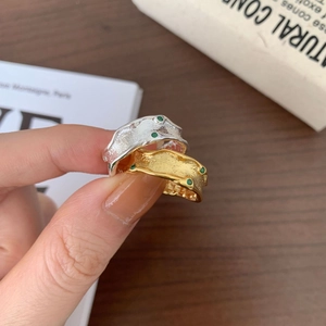 Detailed view of silver and gold irregular wavy rings featuring small green gemstones