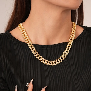 Close-up of a gold-toned Cuban link necklace with pavé-set crystals worn by a model