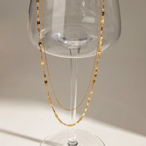 Detail of gold double-layer necklace with Figaro and snake chains on a glass