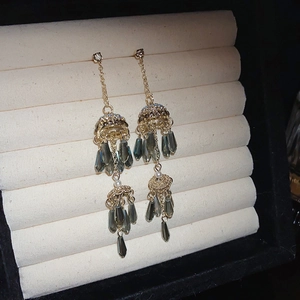 Detailed shot of long gold tassel earrings with dark grey teardrop crystals on a display