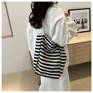 Model wearing a large black and white striped canvas tote bag in a minimalist room