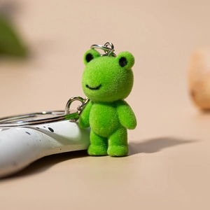 Cute green flocked frog keychain with metal ring and chain on a soft beige background