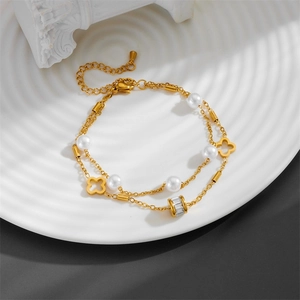 Double-layer gold anklet with hollow clover charm and pearl accents on a white plate