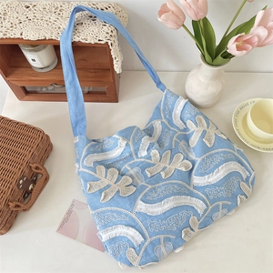 Dettaglio della borsa tote in lino azzurro con ricami floreali a frange e tracolla larga