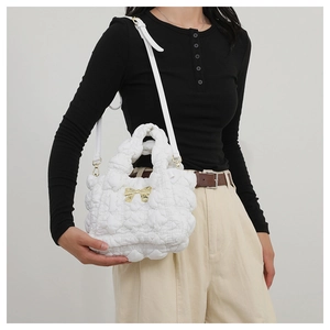 Detailed view of white pleated cloud bag with golden bow and adjustable leather strap