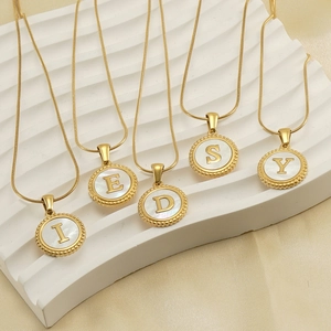 Detail of 18K gold snake chain necklaces with round mother of pearl alphabet pendants