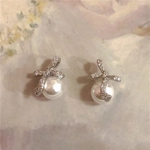 Detail of silver bow earrings with white pearls and sparkling zircons on floral fabric
