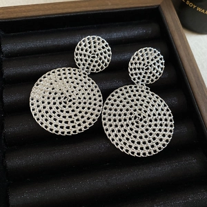 Macro detail of silver hollow circular earrings with intricate woven texture on black velvet