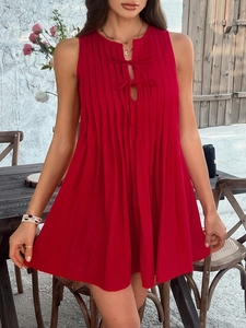 Detail of red sleeveless pleated mini dress with tie-neck design in outdoor setting