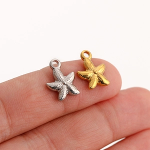 Detailed view of gold and silver starfish pendants resting on a person's fingertip