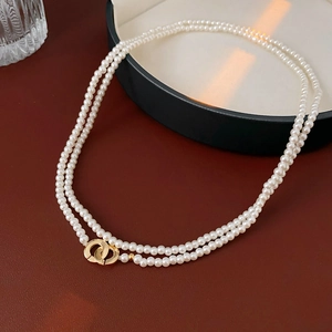 Detail of double-layer pearl necklace featuring a golden interlocking circular clasp