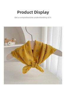 Detail of yellow cotton baby bandana bib with black smiley prints on wooden hanger