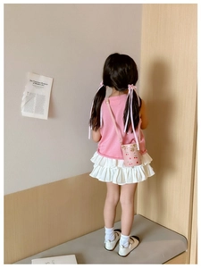 Pink bucket bag with cherry print and golden chain strap worn by a young girl