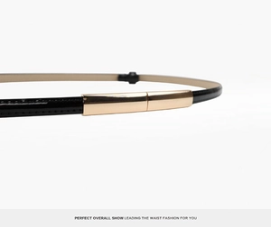 Detail shot of a slim black patent leather belt with a minimalist light gold metal buckle