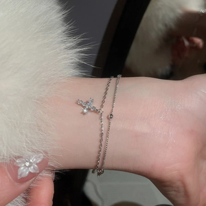 Close-up of a delicate silver double-layered bracelet with a sparkling zircon cross charm