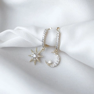 Close-up of asymmetric star and crescent moon earrings with cubic zirconia on white silk