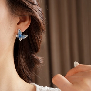 Primer plano de pendientes de mariposa con cristales azules y blancos en la oreja