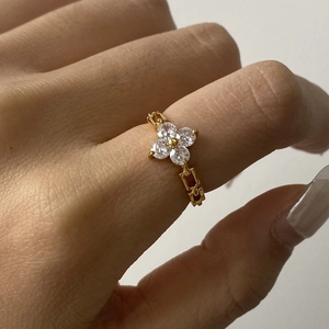 Detail showing a gold clover ring with white zircon stones worn on a woman's finger