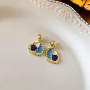 Retro enamel pebble earrings with gold trim and pearl flower accents on a white plate