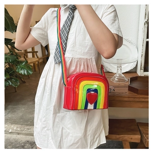 Rainbow crossbody bag featuring a glossy red heart and striped woven shoulder strap