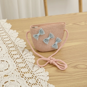 Close-up of pink woven straw crossbody bag with delicate light blue lace bows