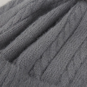 Gros plan d'un bonnet gris en maille torsadée montrant la texture douce et les fils épais