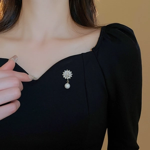 Close-up of gold plated flower brooch with zircon petals and white pearl on a black dress
