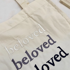 Detailed close-up of multi-colored 'beloved' embroidery on cream canvas tote bag