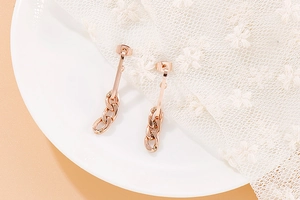 Detailed top view of rose gold Cuban link drop earrings on a white ceramic plate