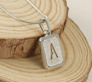 Macro detail of silver stainless steel square pendant with letter A on wood surface
