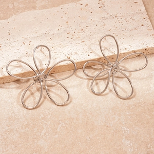 Detail of silver twisted metal flower earrings on a textured cream stone surface