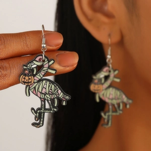 Detailed macro view of flamingo mummy earrings with pumpkin accents and wood texture