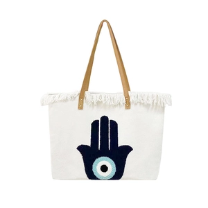 White canvas tote with brown straps featuring a blue Hamsa Hand towel embroidery
