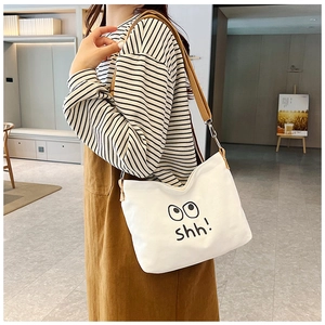 Detailed side view of canvas shoulder bag with cartoon eye print and yellow strap on model
