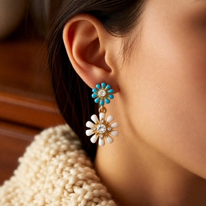 Détail de boucles d'oreilles fleuries avec marguerites bleues et blanches sur modèle