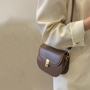 Minimalist brown matte leather saddle bag with gold buckle worn on a shoulder