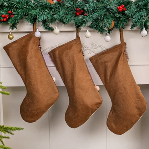 Trois chaussettes de Noël en daim marron sur cheminée avec branches de pin et baies rouges