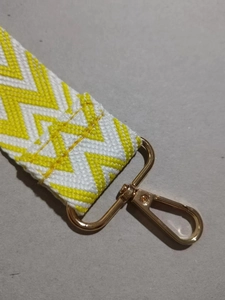Detail der gelb-weißen gewebten Taschengurt mit poliertem goldenem Karabinerhaken