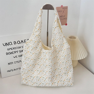 Detail view of cream floral canvas tote bag with yellow daisies hanging on a metal stand