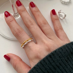 Close-up of gold and silver knot design rings worn with a green knitted sweater