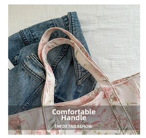 Close-up of wide reinforced carry handles on a floral canvas tote bag with neat stitching