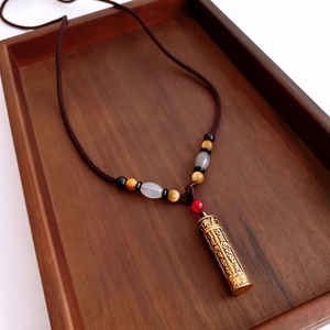 Detailed view of golden cylindrical pendant with script on tiger eye beaded necklace