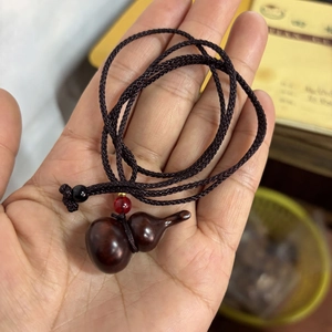 Macro detail of polished rosewood gourd pendant with black woven cord and red accent bead
