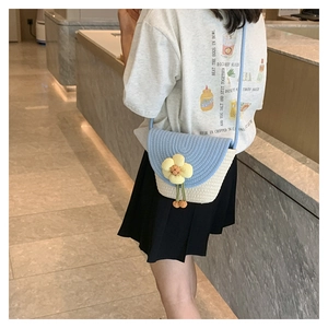 Detalle de bolso tipo cubo de paja tejida a mano con solapa azul y flor 3D amarilla
