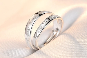 Detail of silver couple rings with Love Forever engraving on soft white fabric background
