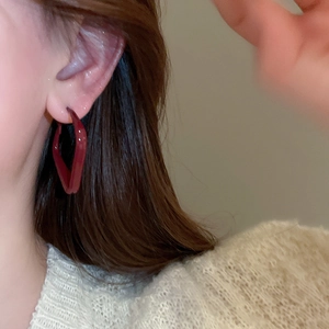 Close-up of a woman wearing geometric deep red lacquer earrings with a glossy finish
